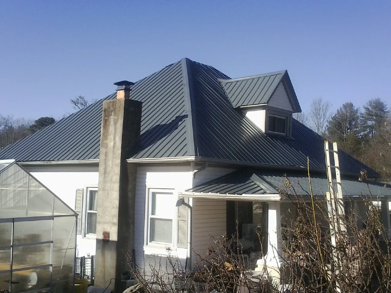 Dark blue standing seam metal roof on a white farmhouse with dormer — Slate & Tile Roof Repair by Roofing Brothers in Huntington Mills
