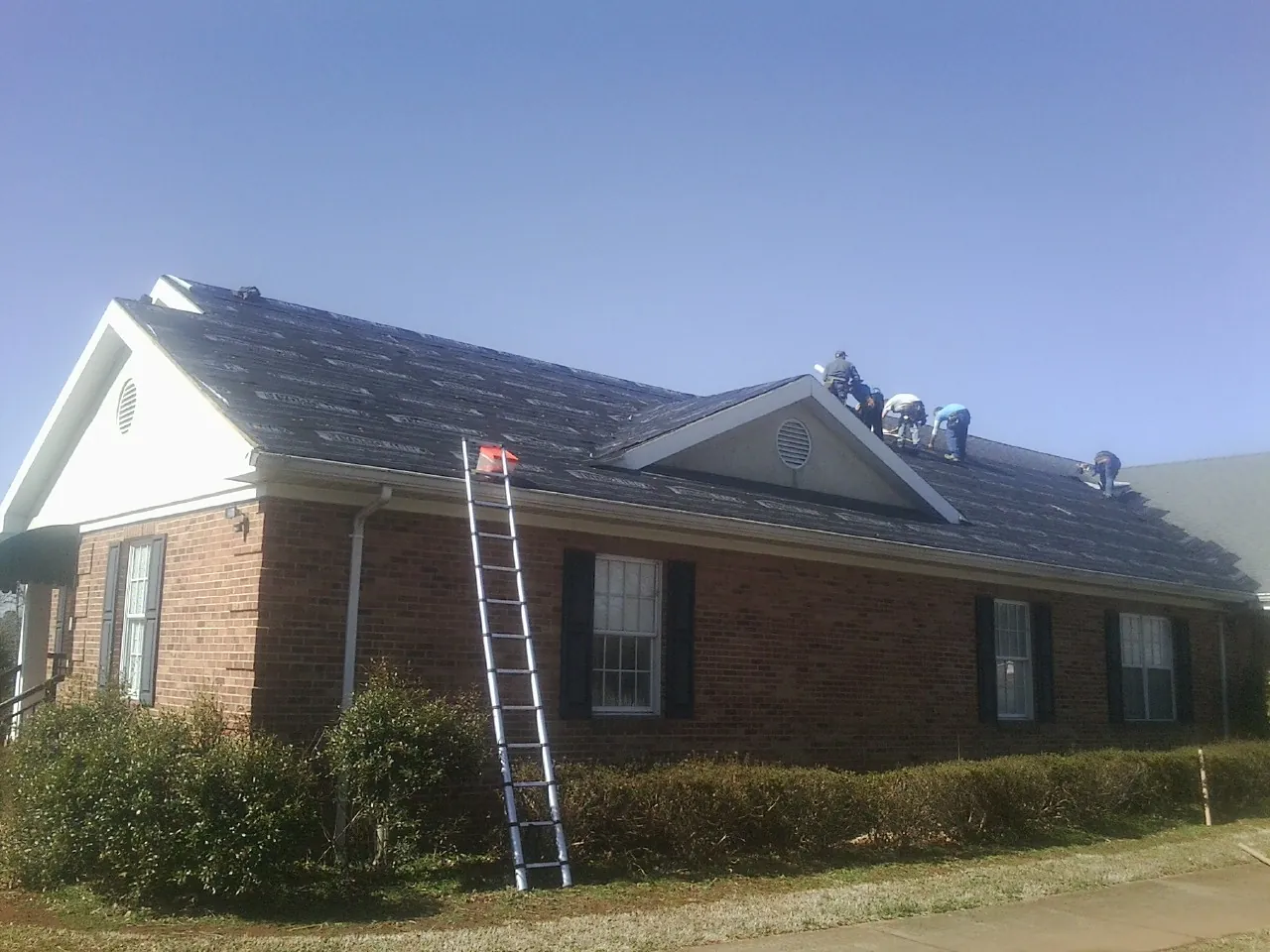 Crew tearing shingles off a brick ranch roof with a ladder set — Metal Roof Repair work by our crew in Huntington Mills
