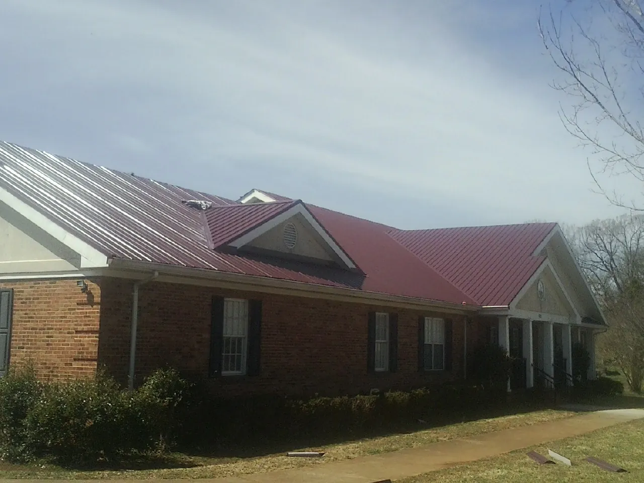 Red metal roof with gabled entries on a long brick building, from a Hail Damage Roof Repair job in Huntington Mills