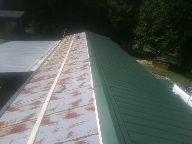 Old rusted panels beside newly installed green metal roofing — Wind Damage Roof Repair by Roofing Brothers in Huntington Mills