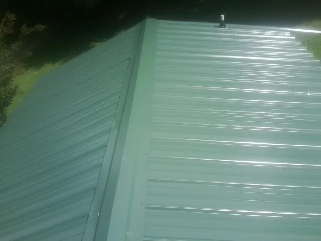 New green metal panels meeting at the ridge of a roof — Flat Roof Repair work by our crew in Huntington Mills