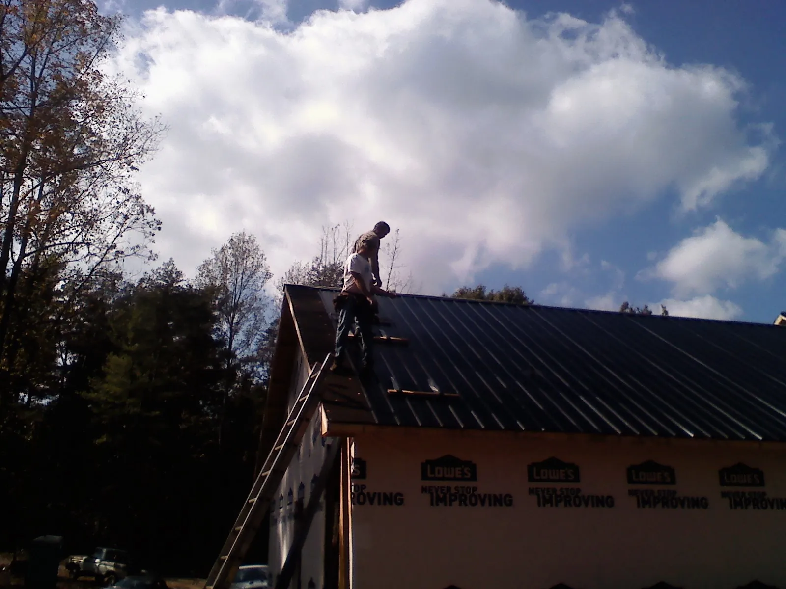 Roofer fastening dark metal panels high against a cloudy sky, from a Roof Inspection job in Huntington Mills