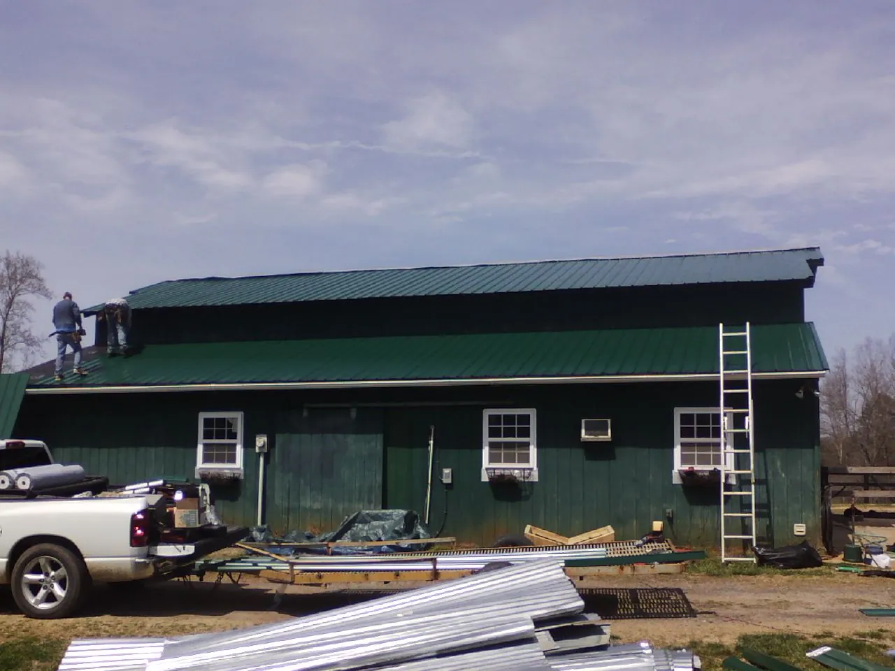Crew installing green metal roofing on a large green barn in Huntington Mills