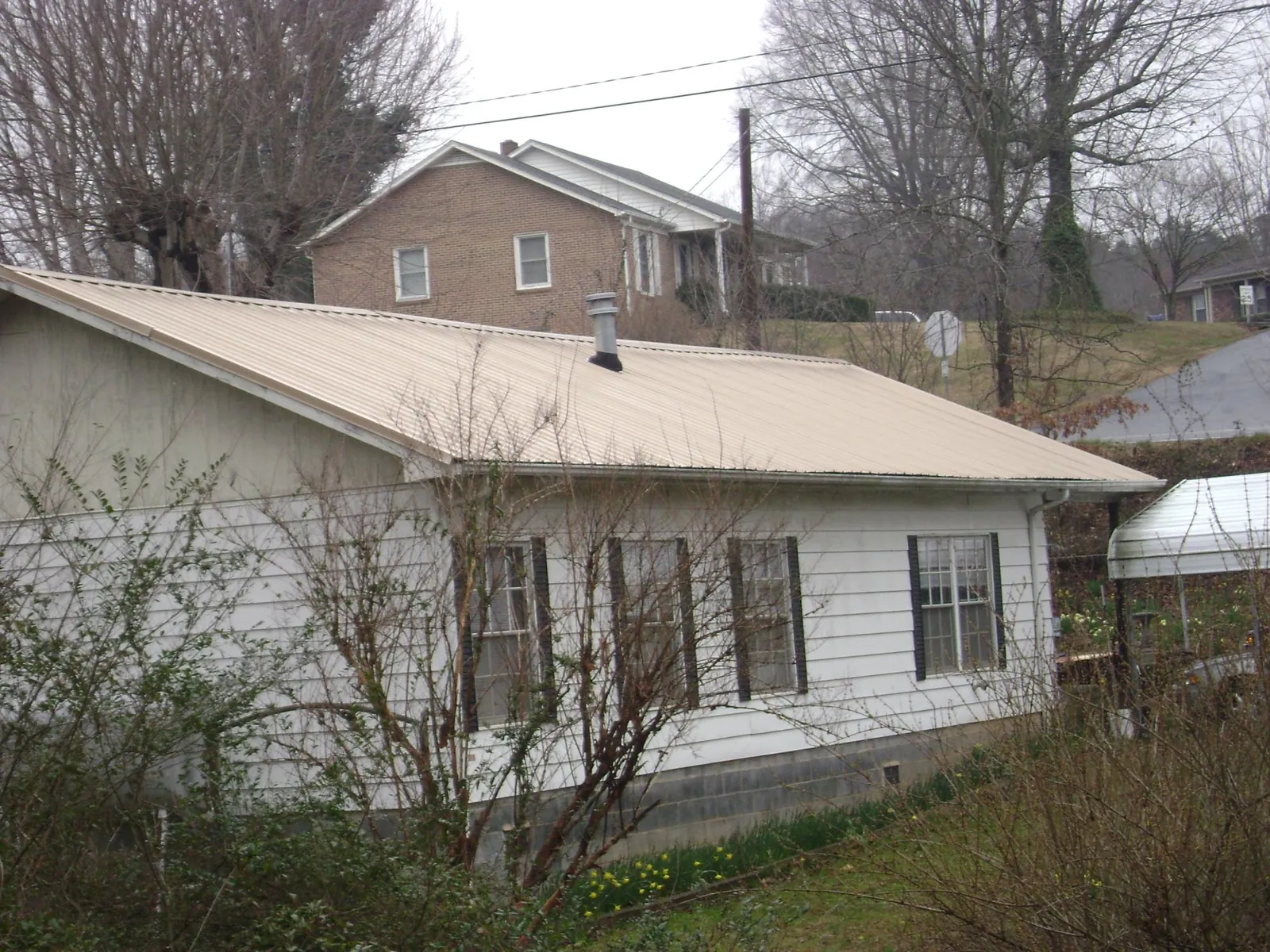 Tan metal roof on a white sided house set into a hillside — Commercial Roofing by Roofing Brothers in Huntington Mills