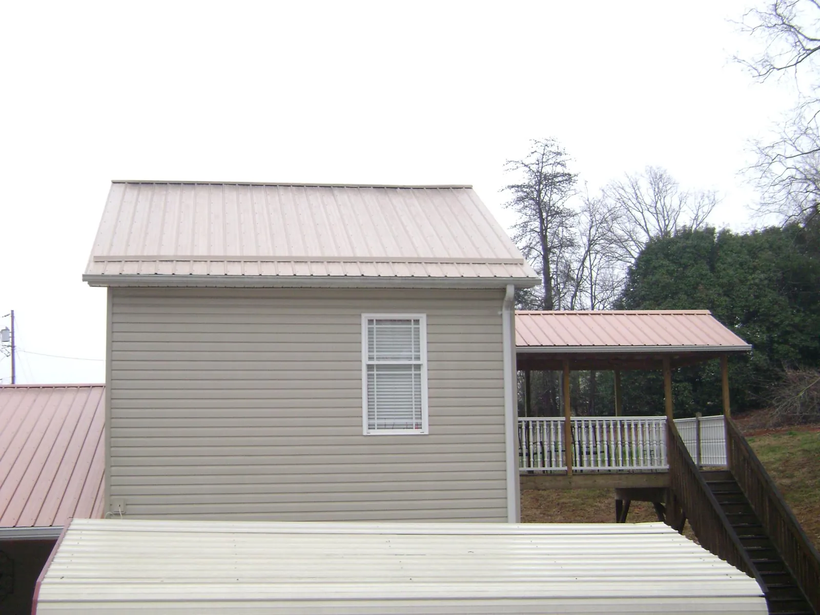 Tan metal roofs on a two story addition and attached porch, from a Roof Replacement job in Huntington Mills