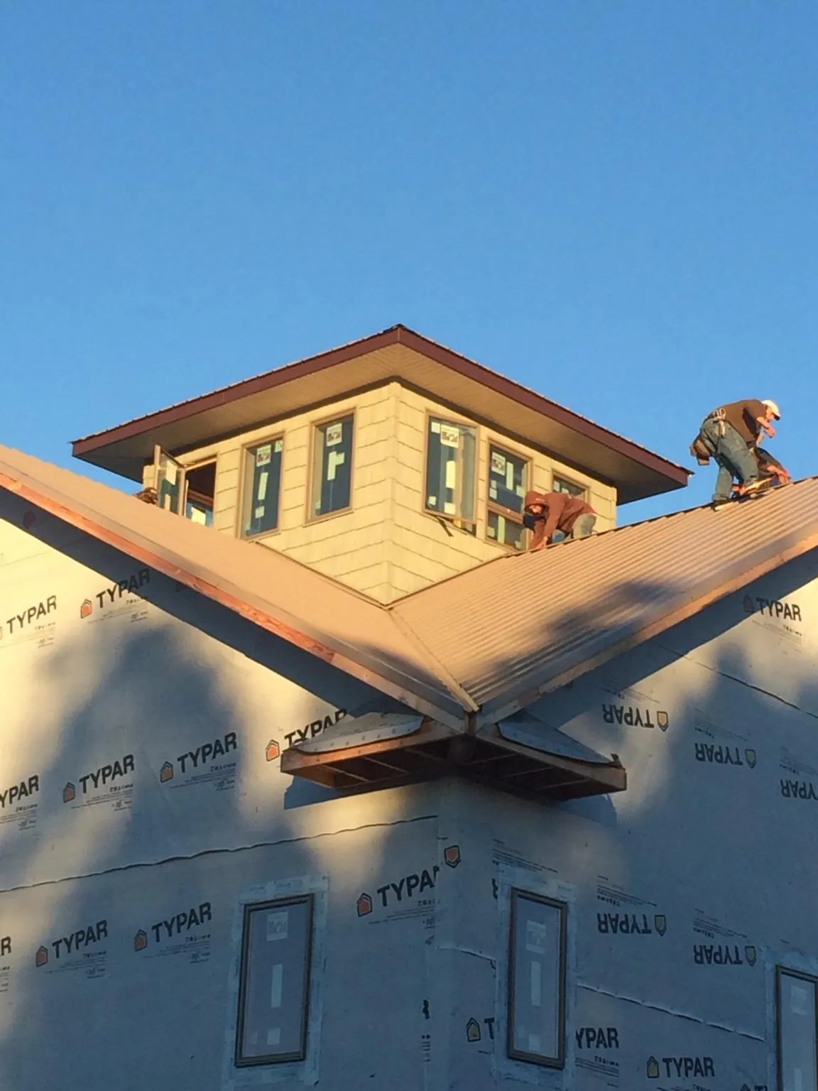 Roofers working around a rooftop cupola on a new metal roof at sunset — Roof Waterproofing in Huntington Mills by Roofing Brothers